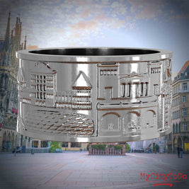 Silberner Ring mit Reliefs bekannter Sehenswürdigkeiten der Stadt Muenchen. Den Hintergrund bildet eine Ansicht der Stadt Muenchen.