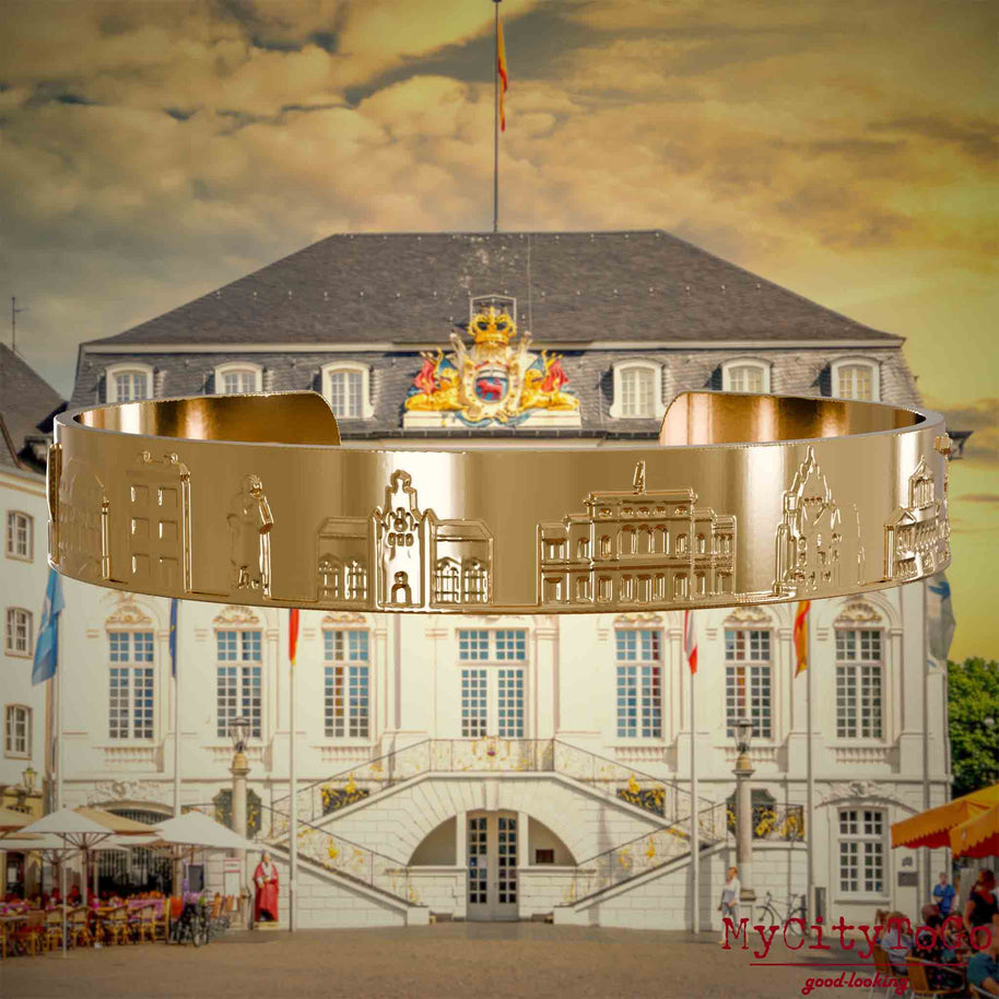 Vergoldeter Armreif mit Reliefs bekannter Sehenswürdigkeiten der Stadt Bonn. Den Hintergrund bildet eine Ansicht der Stadt Bonn.