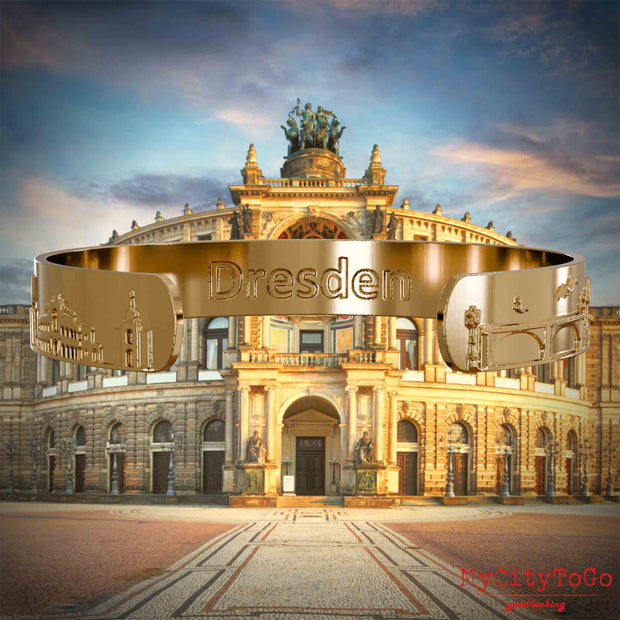 Innenseite eines vergoldeten Armreifs mit Reliefs bekannter Sehenswürdigkeiten der Stadt Dresden und einer Gravur des Stadtnamens. Den Hintergrund bildet eine Ansicht der Stadt Dresden.