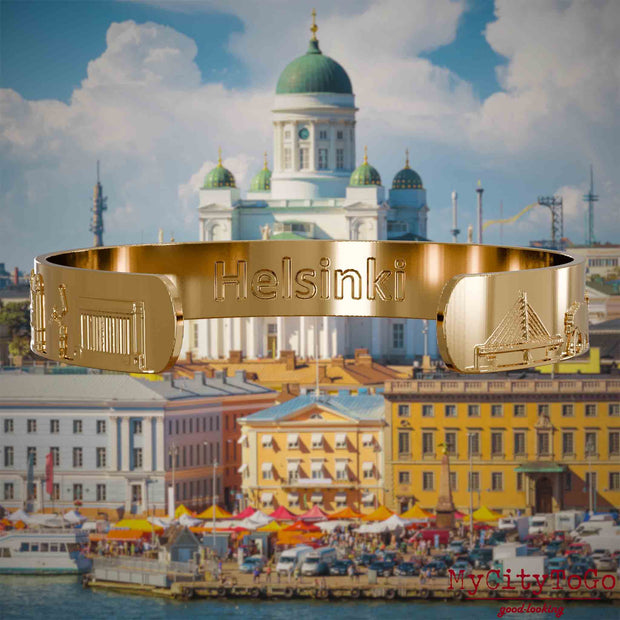 Innenseite eines vergoldeten Armreifs mit Reliefs bekannter Sehenswürdigkeiten der Stadt Helsinki und einer Gravur des Stadtnamens. Den Hintergrund bildet eine Ansicht der Stadt Helsinki.