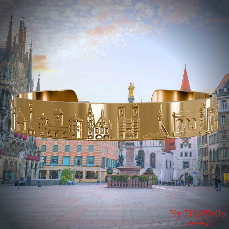 Vergoldeter Armreif mit Reliefs bekannter Sehenswürdigkeiten der Stadt München. Den Hintergrund bildet eine Ansicht der Stadt Muenchen.