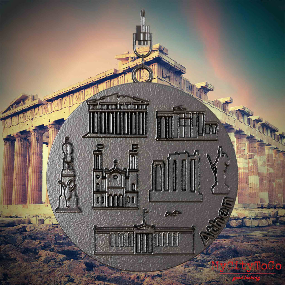 Halskette mit Drehwirbel und Vorderseite eines Schmuckanhängers aus Titan, auf dem Reliefs bekannter Sehenswürdigkeiten der Stadt Athen abgebildet sind. Den Hintergrund bildet eine Ansicht der Stadt Athen.

