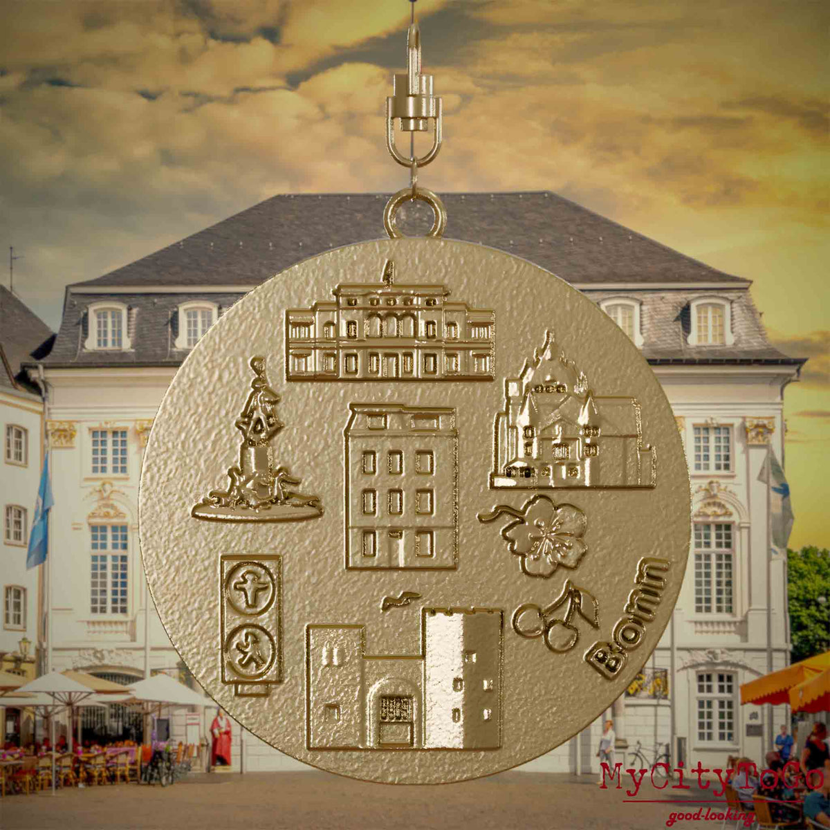 Halskette mit Drehwirbel und Rückseite eines Schmuckanhängers aus vergoldetem Edelstahl, auf dem Reliefs bekannter Sehenswürdigkeiten der Stadt Bonn abgebildet sind. Den Hintergrund bildet eine Ansicht der Stadt Bonn.
