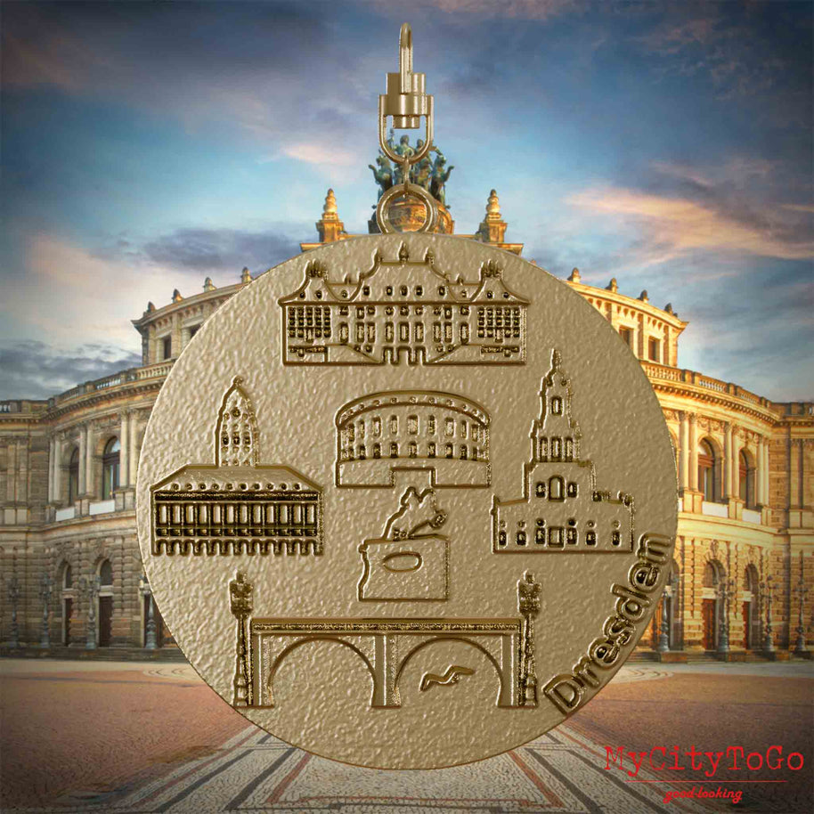 Halskette mit Drehwirbel und Vorderseite eines Schmuckanhängers aus vergoldetem Edelstahl, auf dem Reliefs bekannter Sehenswürdigkeiten der Stadt Dresden abgebildet sind. Den Hintergrund bildet eine Ansicht der Stadt Dresden.