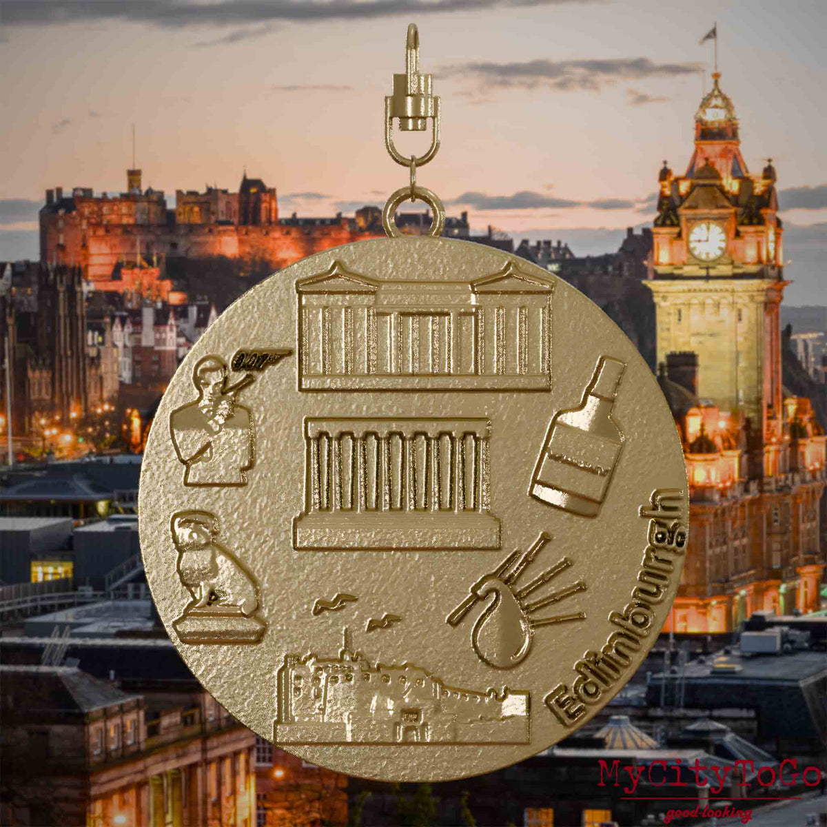 Halskette mit Drehwirbel und Vorderseite eines Schmuckanhängers aus vergoldetem Edelstahl, auf dem Reliefs bekannter Sehenswürdigkeiten der Stadt Edinburgh abgebildet sind. Den Hintergrund bildet eine Ansicht der Stadt Edinburgh.
