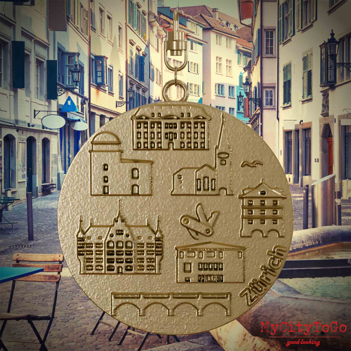 Halskette mit Drehwirbel und Rückseite eines Schmuckanhängers aus vergoldetem Edelstahl, auf dem Reliefs bekannter Sehenswürdigkeiten der Stadt Zuerich abgebildet sind. Den Hintergrund bildet eine Ansicht der Stadt Zuerich.
