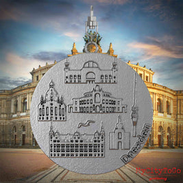 Halskette mit Drehwirbel und Rückseite eines Schmuckanhängers aus Edelstahl, auf dem Reliefs bekannter Sehenswürdigkeiten der Stadt Dresden abgebildet sind. Den Hintergrund bildet eine Ansicht der Stadt Dresden.
