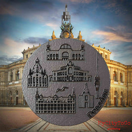 Halskette mit Drehwirbel und Rückseite eines Schmuckanhängers aus Titan, auf dem Reliefs bekannter Sehenswürdigkeiten der Stadt Dresden abgebildet sind. Den Hintergrund bildet eine Ansicht der Stadt Dresden.