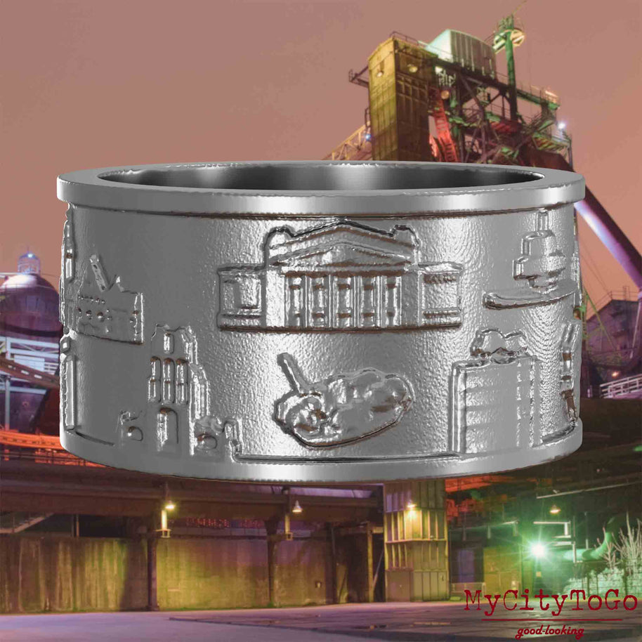 Ring aus Edelstahl mit Reliefs bekannter Sehenswürdigkeiten der Stadt Duisburg. Den Hintergrund bildet eine Ansicht der Stadt Duisburg.