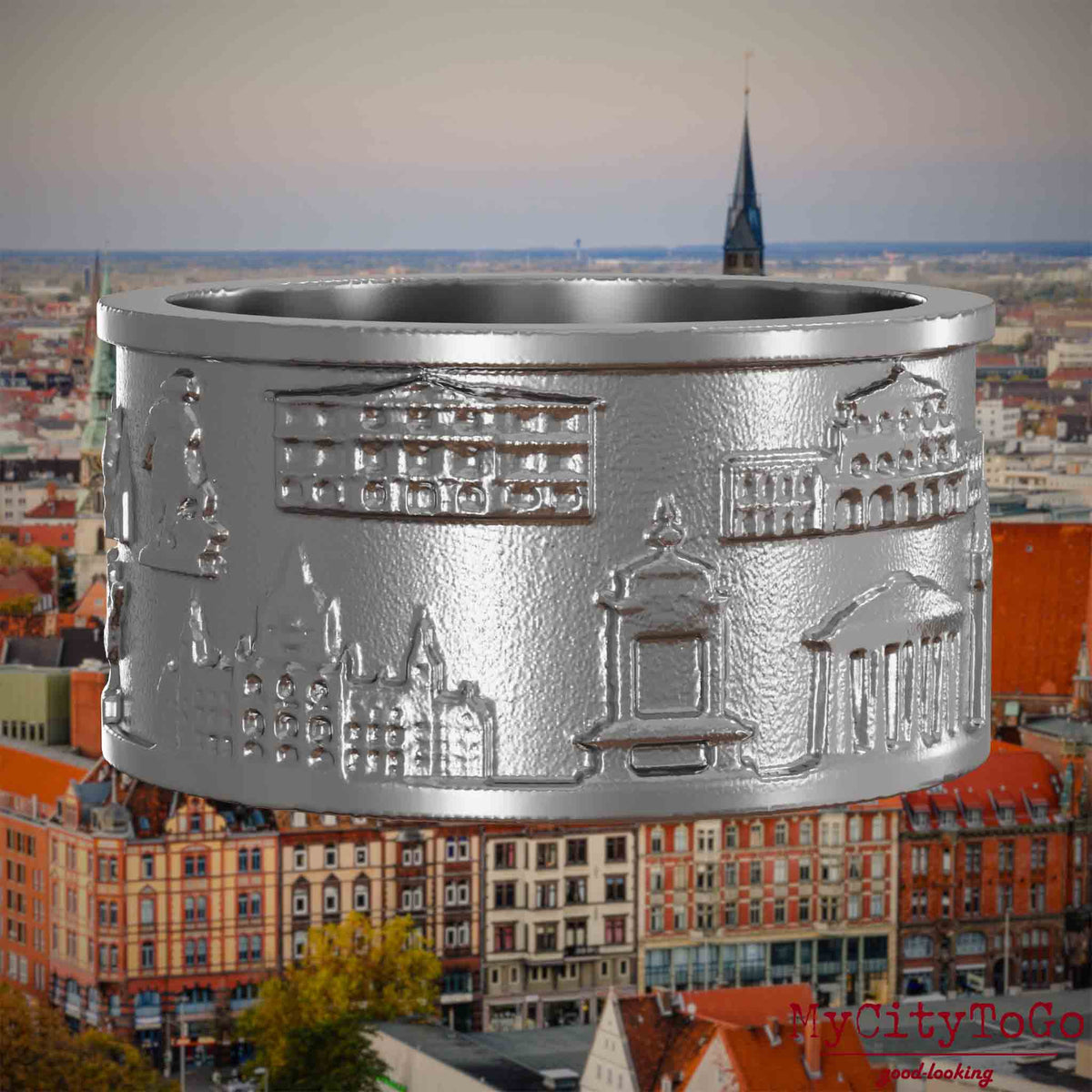 Ring aus Edelstahl mit Reliefs bekannter Sehenswürdigkeiten der Stadt Hannover. Den Hintergrund bildet eine Ansicht der Stadt Hannover.