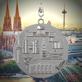 Halskette mit Drehwirbel und Rückseite eines silbernen Schmuckanhängers, auf dem Reliefs bekannter Sehenswürdigkeiten der Stadt Koeln abgebildet sind. Den Hintergrund bildet eine Ansicht der Stadt Koeln.