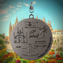 Halskette mit Drehwirbel und Rückseite eines Schmuckanhängers aus Titan, auf dem Reliefs bekannter Sehenswürdigkeiten der Stadt Palma de Mallorca abgebildet sind. Den Hintergrund bildet eine Ansicht der Stadt Palma de Mallorca.
