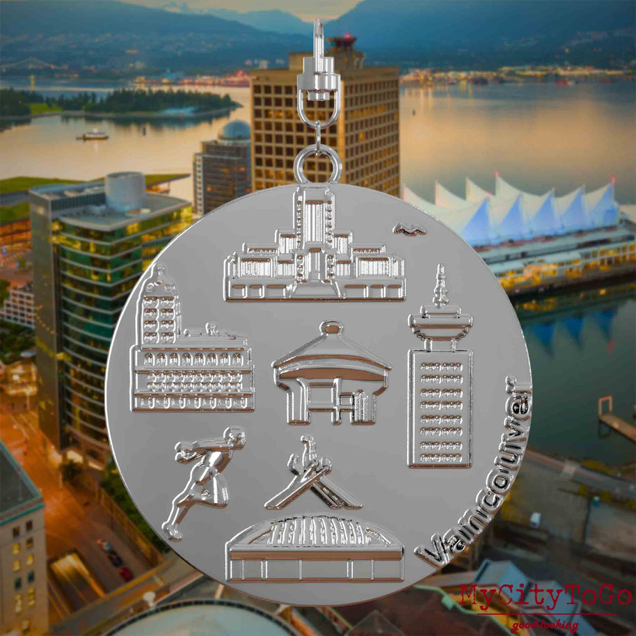 Halskette mit Drehwirbel und Rückseite eines silbernen Schmuckanhängers, auf dem Reliefs bekannter Sehenswürdigkeiten der Stadt Vancouver abgebildet sind. Den Hintergrund bildet eine Ansicht der Stadt Vancouver.
