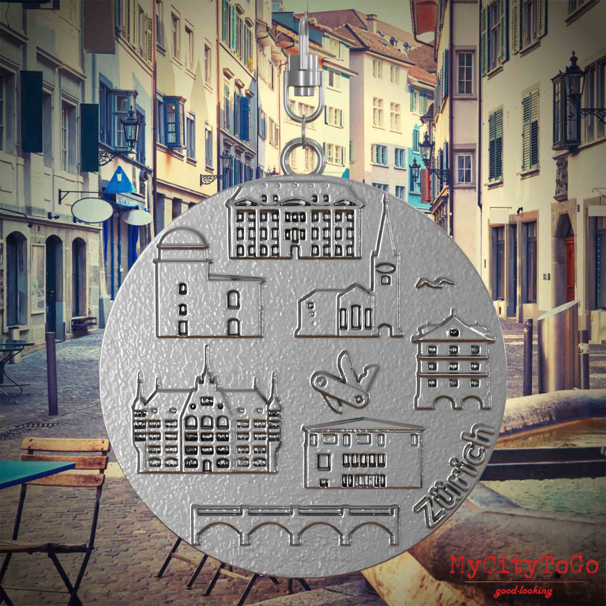 Halskette mit Drehwirbel und Rückseite eines Schmuckanhängers aus Edelstahl, auf dem Reliefs bekannter Sehenswürdigkeiten der Stadt Zuerich abgebildet sind. Den Hintergrund bildet eine Ansicht der Stadt Zuerich.
