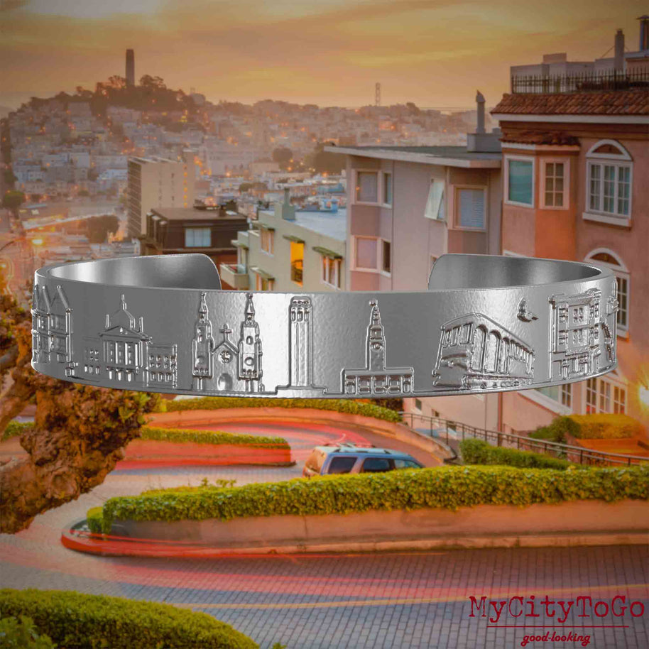 Armreif aus Edelstahl mit Reliefs bekannter Sehenswürdigkeiten der Stadt San Francisco. Den Hintergrund bildet eine Ansicht der Stadt San Francisco.