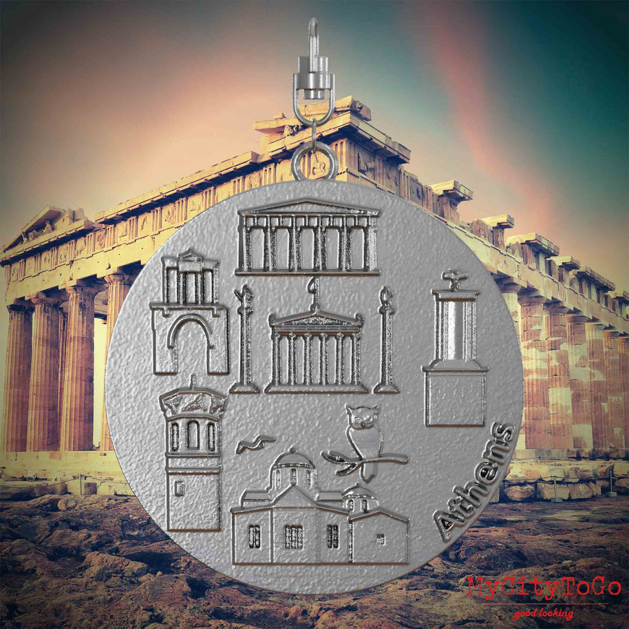 Halskette mit Drehwirbel und Rückseite eines Schmuckanhängers aus Edelstahl, auf dem Reliefs bekannter Sehenswürdigkeiten der Stadt Athen abgebildet sind. Den Hintergrund bildet eine Ansicht der Stadt Athen.
