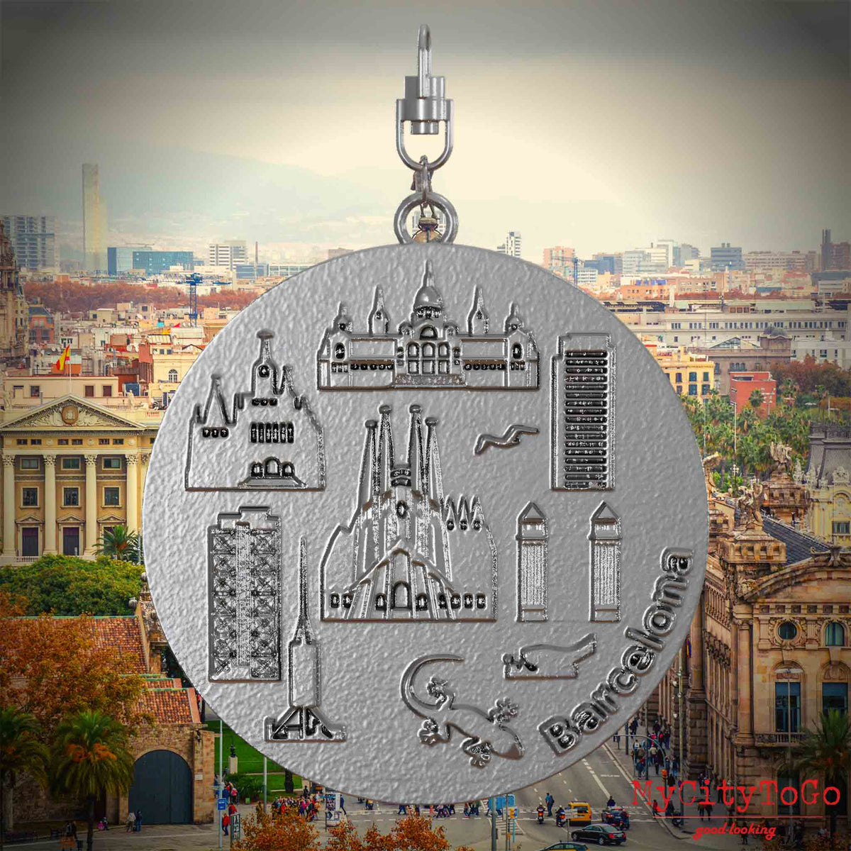 Halskette mit Drehwirbel und Rückseite eines Schmuckanhängers aus Edelstahl, auf dem Reliefs bekannter Sehenswürdigkeiten der Stadt Barcelona abgebildet sind. Den Hintergrund bildet eine Ansicht der Stadt Barcelona.

