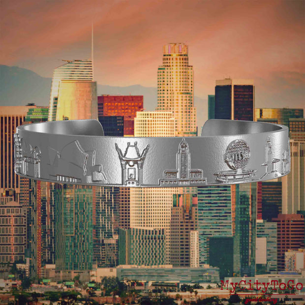 Armreif aus Edelstahl mit Reliefs bekannter Sehenswürdigkeiten der Stadt Los Angeles. Den Hintergrund bildet eine Ansicht der Stadt Los Angeles.