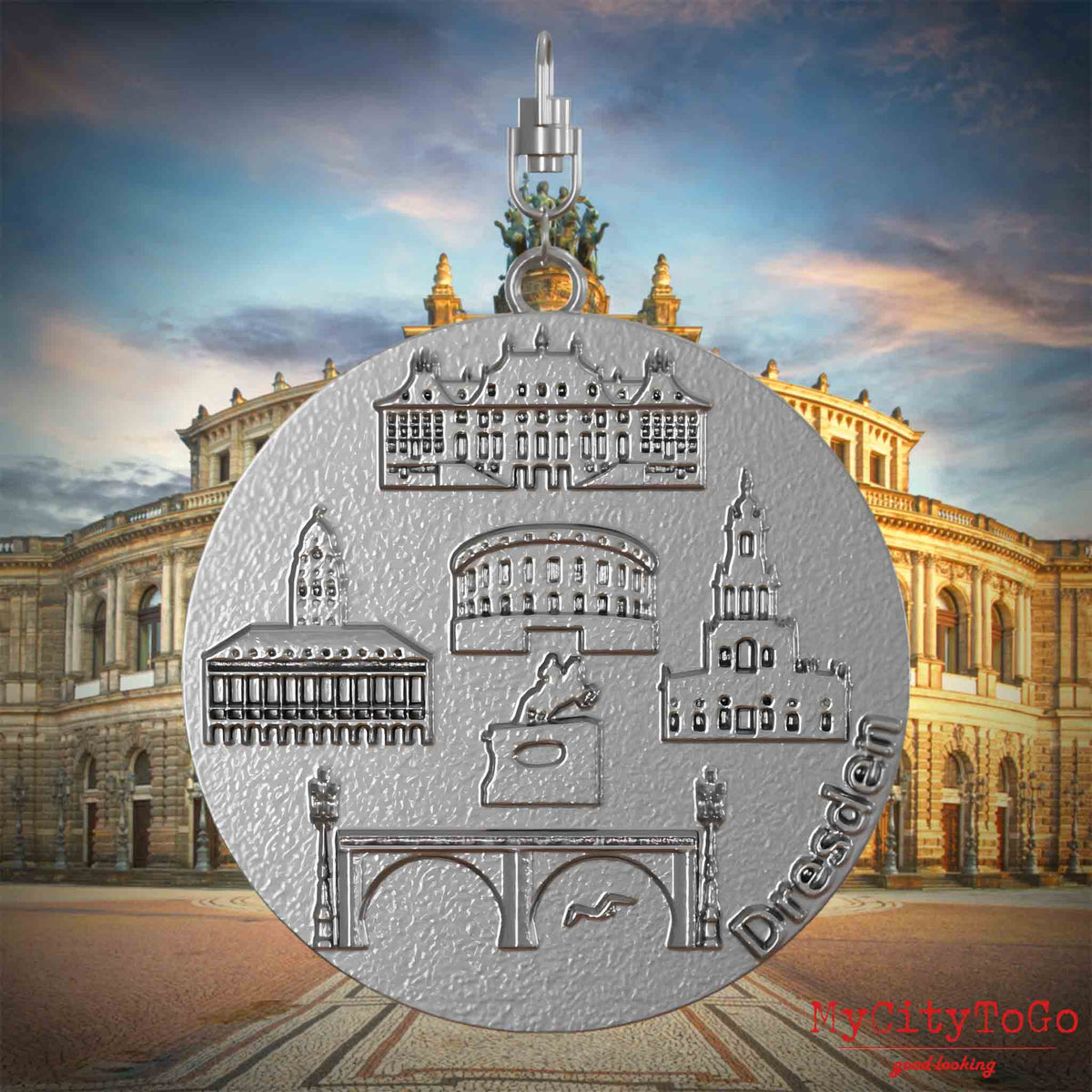 Halskette mit Drehwirbel und Vorderseite eines Schmuckanhängers aus Edelstahl, auf dem Reliefs bekannter Sehenswürdigkeiten der Stadt Dresdenabgebildet sind. Den Hintergrund bildet eine Ansicht der Stadt Dresden.