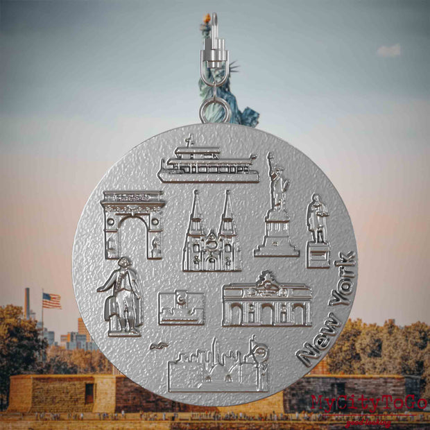 Halskette mit Drehwirbel und Vorderseite eines Schmuckanhängers aus Edelstahl, auf dem Reliefs bekannter Sehenswürdigkeiten der Stadt New York abgebildet sind. Den Hintergrund bildet eine Ansicht der Stadt New York.
