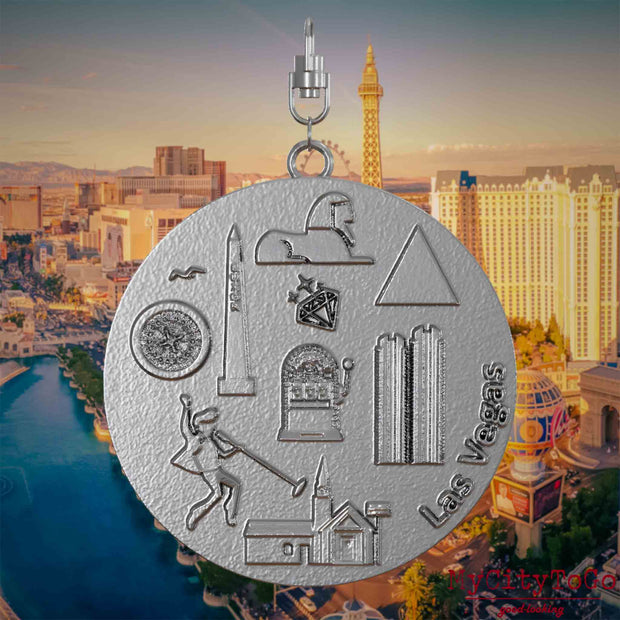 Halskette mit Drehwirbel und Vorderseite eines Schmuckanhängers aus Edelstahl, auf dem Reliefs bekannter Sehenswürdigkeiten der Stadt Las Vegas abgebildet sind. Den Hintergrund bildet eine Ansicht der Stadt Las Vegas.
