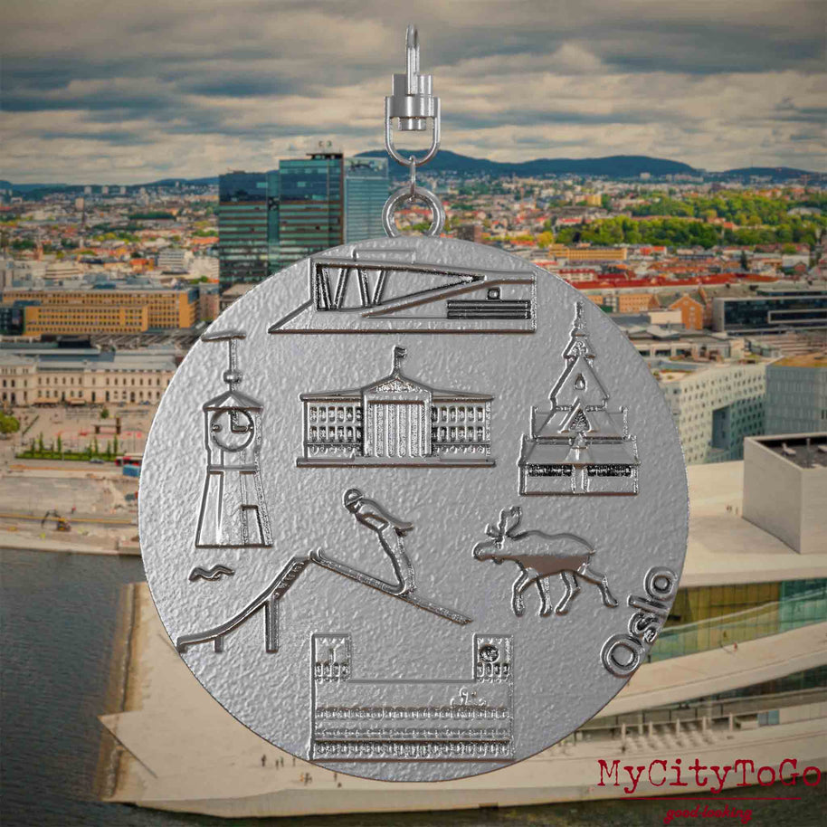 Halskette mit Drehwirbel und Vorderseite eines Schmuckanhängers aus Edelstahl, auf dem Reliefs bekannter Sehenswürdigkeiten der Stadt Oslo abgebildet sind. Den Hintergrund bildet eine Ansicht der Stadt Oslo.
