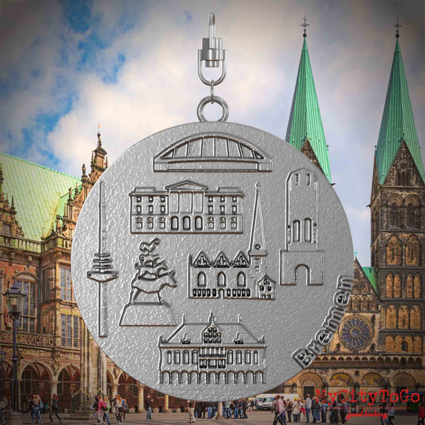 Halskette mit Drehwirbel und Vorderseite eines Schmuckanhängers aus Edelstahl, auf dem Reliefs bekannter Sehenswürdigkeiten der Stadt Bremen abgebildet sind. Den Hintergrund bildet eine Ansicht der Stadt Bremen.