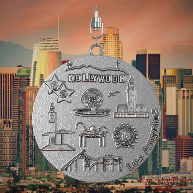 Halskette mit Drehwirbel und Vorderseite eines Schmuckanhängers aus Edelstahl, auf dem Reliefs bekannter Sehenswürdigkeiten der Stadt Los Angeles abgebildet sind. Den Hintergrund bildet eine Ansicht der Stadt Los Angeles.
