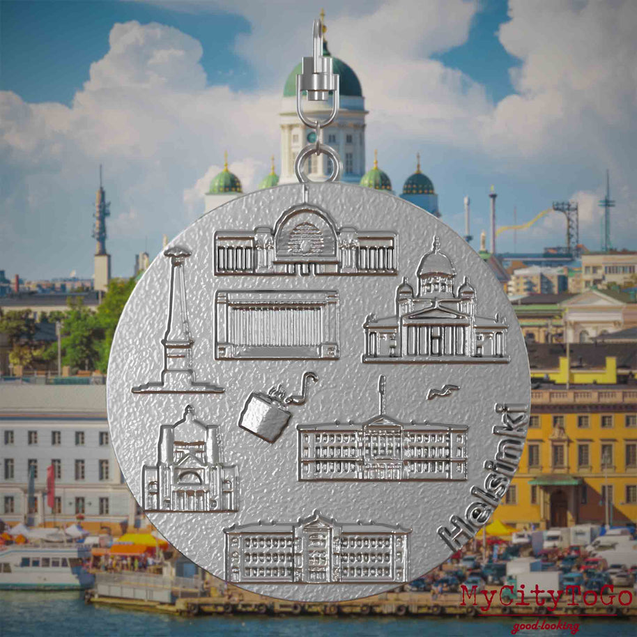Halskette mit Drehwirbel und Vorderseite eines Schmuckanhängers aus Edelstahl, auf dem Reliefs bekannter Sehenswürdigkeiten der Stadt Helsinki abgebildet sind. Den Hintergrund bildet eine Ansicht der Stadt Helsinki.
