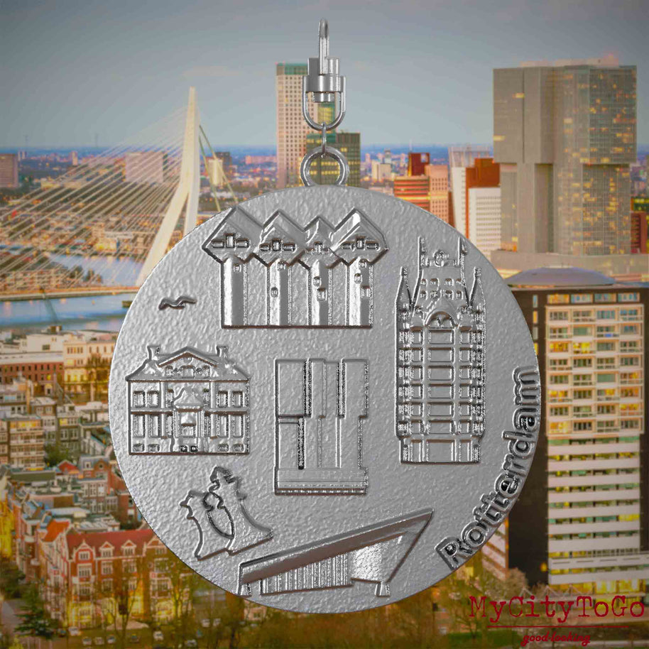 Halskette mit Drehwirbel und Vorderseite eines Schmuckanhängers aus Edelstahl, auf dem Reliefs bekannter Sehenswürdigkeiten der Stadt Rotterdam abgebildet sind. Den Hintergrund bildet eine Ansicht der Stadt Rotterdam.


