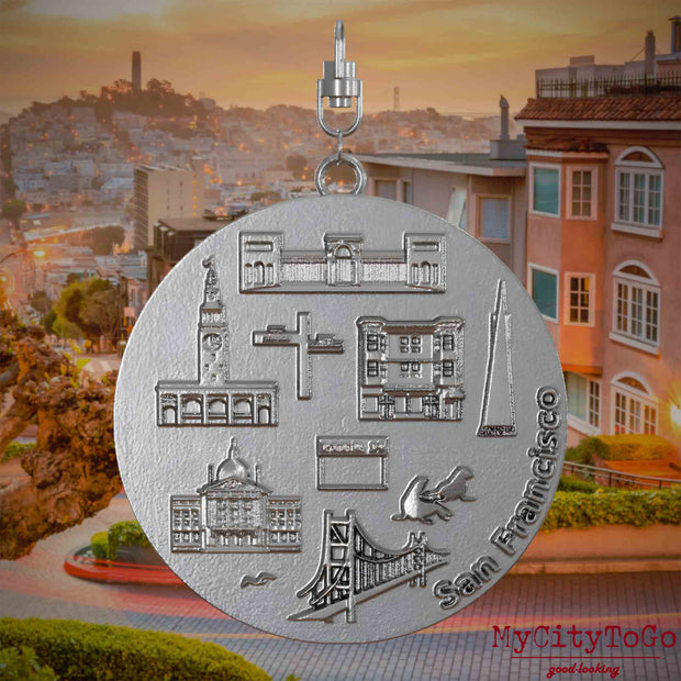 Halskette mit Drehwirbel und Vorderseite eines Schmuckanhängers aus Edelstahl, auf dem Reliefs bekannter Sehenswürdigkeiten der Stadt San Francisco abgebildet sind. Den Hintergrund bildet eine Ansicht der Stadt San Francisco.
