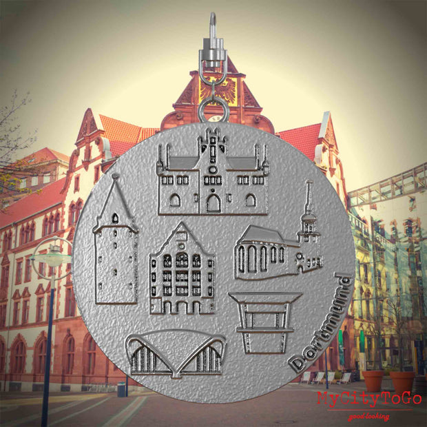 Halskette mit Drehwirbel und Rückseite eines Schmuckanhängers aus Edelstahl, auf dem Reliefs bekannter Sehenswürdigkeiten der Stadt Dortmund abgebildet sind. Den Hintergrund bildet eine Ansicht der Stadt Dortmund.