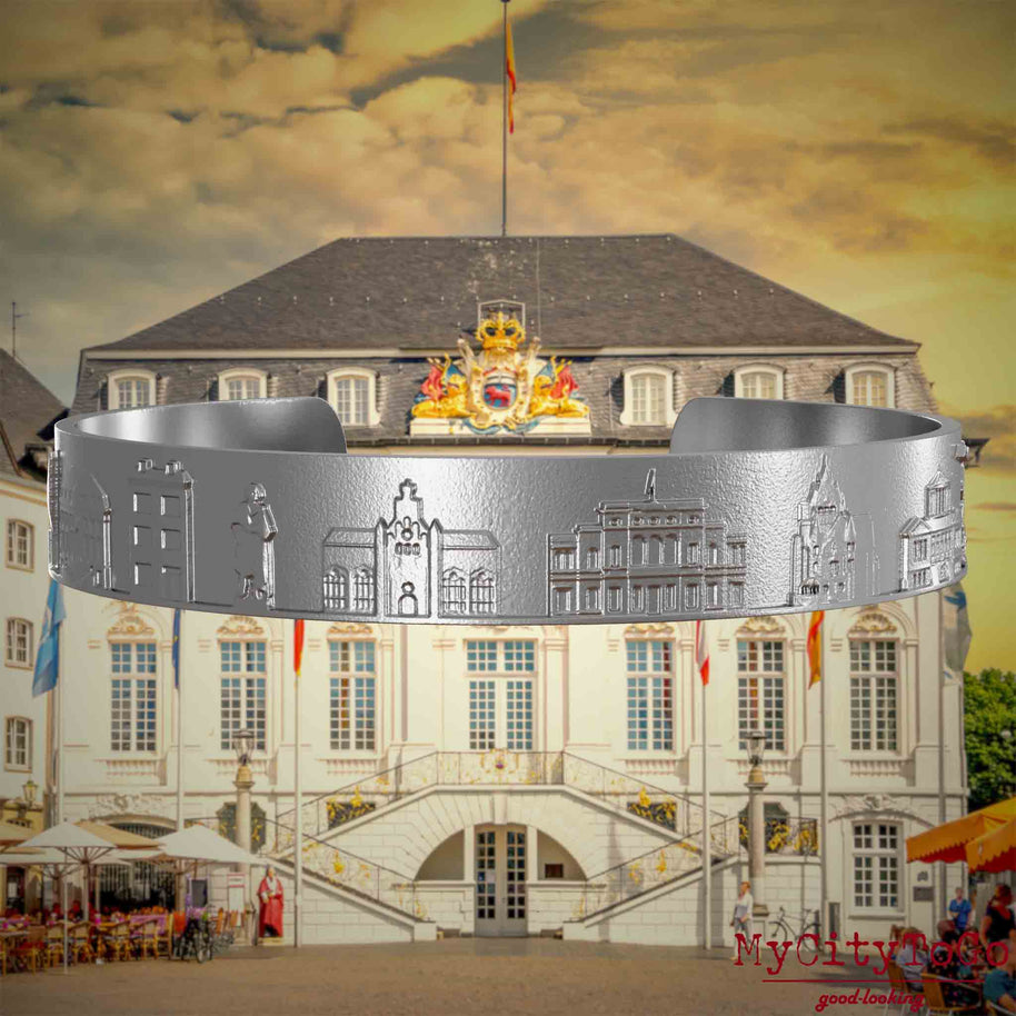 Armreif aus Edelstahl mit Reliefs bekannter Sehenswürdigkeiten der Stadt Bonn. Den Hintergrund bildet eine Ansicht der Stadt Bonn.