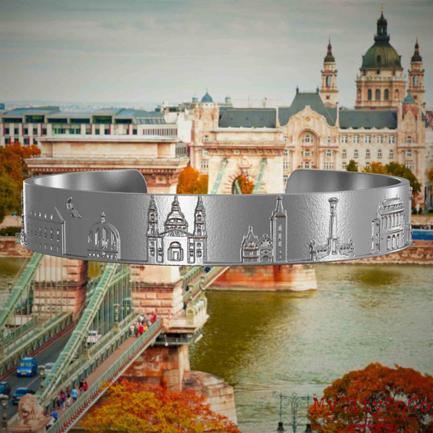 Armreif aus Edelstahl mit Reliefs bekannter Sehenswürdigkeiten der Stadt Budapest. Den Hintergrund bildet eine Ansicht der Stadt Budapest.