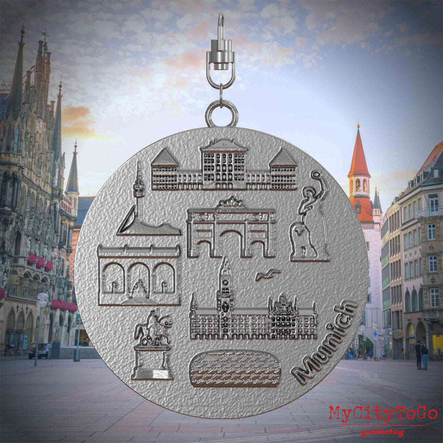 Halskette mit Drehwirbel und Rückseite eines Schmuckanhängers aus Edelstahl, auf dem Reliefs bekannter Sehenswürdigkeiten der Stadt Muenchen abgebildet sind. Den Hintergrund bildet eine Ansicht der Stadt Muenchen.