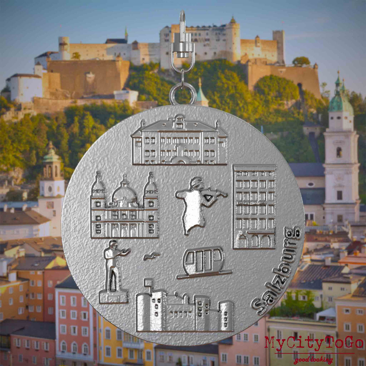 Halskette mit Drehwirbel und Vorderseite eines Schmuckanhängers aus Edelstahl, auf dem Reliefs bekannter Sehenswürdigkeiten der Stadt Salzburg abgebildet sind. Den Hintergrund bildet eine Ansicht der Stadt Salzburg.
