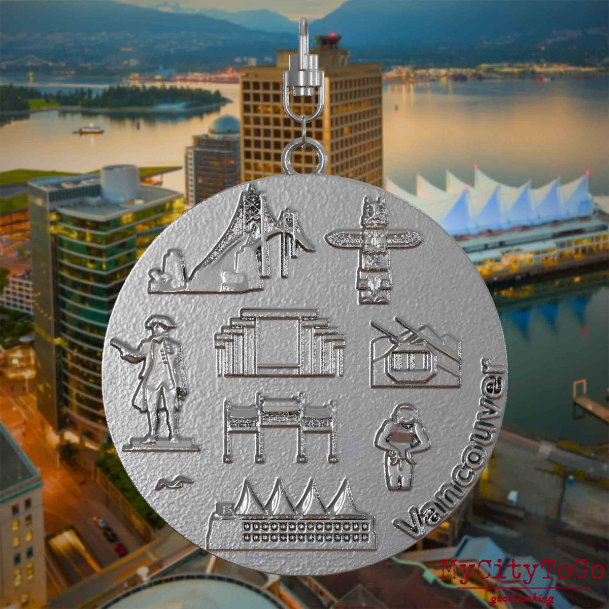 Halskette mit Drehwirbel und Vorderseite eines Schmuckanhängers aus Edelstahl, auf dem Reliefs bekannter Sehenswürdigkeiten der Stadt Vancouver abgebildet sind. Den Hintergrund bildet eine Ansicht der Stadt Vancouver.

