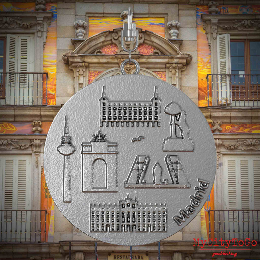 Halskette mit Drehwirbel und Vorderseite eines Schmuckanhängers aus Edelstahl, auf dem Reliefs bekannter Sehenswürdigkeiten der Stadt Madrid abgebildet sind. Den Hintergrund bildet eine Ansicht der Stadt Madrid.
