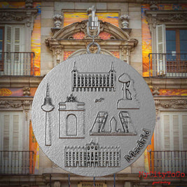 Halskette mit Drehwirbel und Vorderseite eines Schmuckanhängers aus Edelstahl, auf dem Reliefs bekannter Sehenswürdigkeiten der Stadt Madrid abgebildet sind. Den Hintergrund bildet eine Ansicht der Stadt Madrid.
