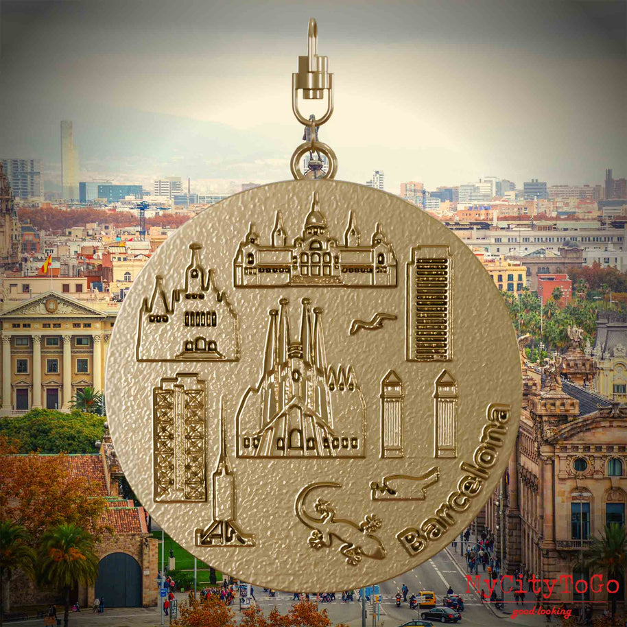 Halskette mit Drehwirbel und Rückseite eines Schmuckanhängers aus vergoldetem Edelstahl, auf dem Reliefs bekannter Sehenswürdigkeiten der Stadt Barcelona abgebildet sind. Den Hintergrund bildet eine Ansicht der Stadt Barcelona.
