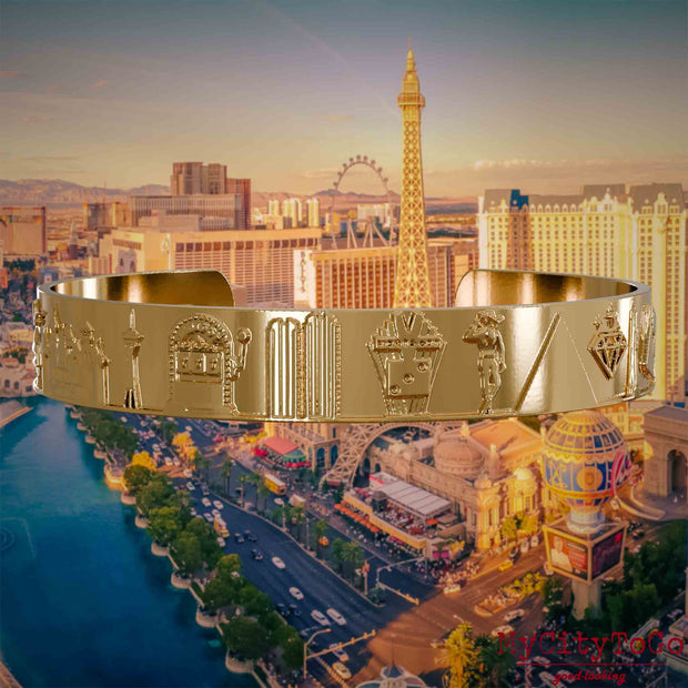Vergoldeter Armreif mit Reliefs bekannter Sehenswürdigkeiten der Stadt Las Vegas. Den Hintergrund bildet eine Ansicht der Stadt Las Vegas.