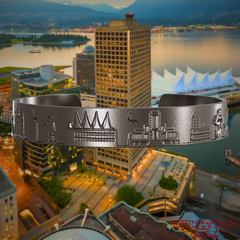 Armreif aus Titan mit Reliefs bekannter Sehenswürdigkeiten der Stadt Vancouver. Den Hintergrund bildet eine Ansicht der Stadt Vancouver.