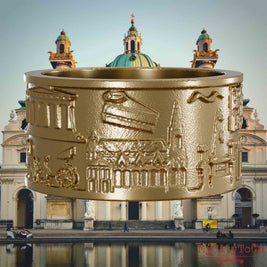 Ring aus vergoldetem Edelstahl mit Reliefs bekannter Sehenswürdigkeiten der Stadt Wien. Den Hintergrund bildet eine Ansicht der Stadt Wien.