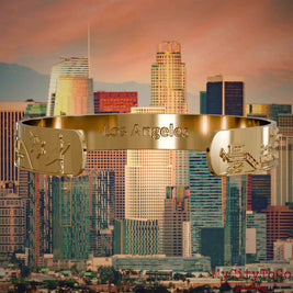 Innenseite eines vergoldeten Armreifs mit Reliefs bekannter Sehenswürdigkeiten der Stadt Los Angeles und einer Gravur des Stadtnamens. Den Hintergrund bildet eine Ansicht der Stadt Los Angeles.