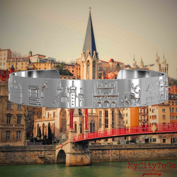Versilberter Armreif mit Reliefs bekannter Sehenswürdigkeiten der Stadt Lyon. Den Hintergrund bildet eine Ansicht der Stadt Lyon.