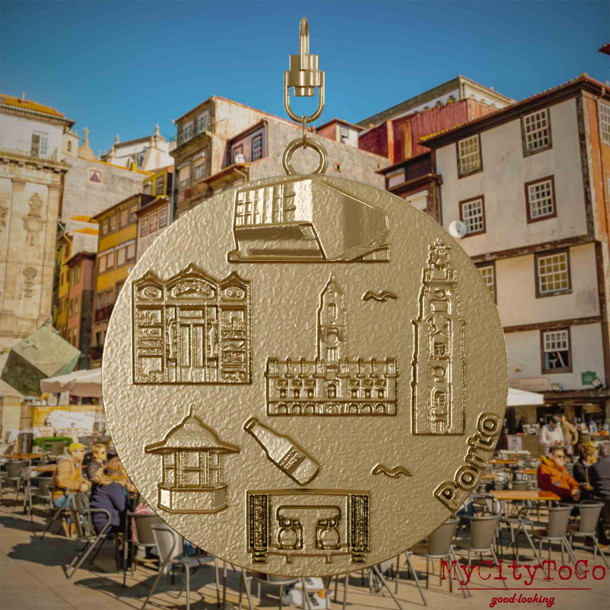 Halskette mit Drehwirbel und Vorderseite eines Schmuckanhängers aus vergoldetem Edelstahl, auf dem Reliefs bekannter Sehenswürdigkeiten der Stadt Porto abgebildet sind. Den Hintergrund bildet eine Ansicht der Stadt Porto.
