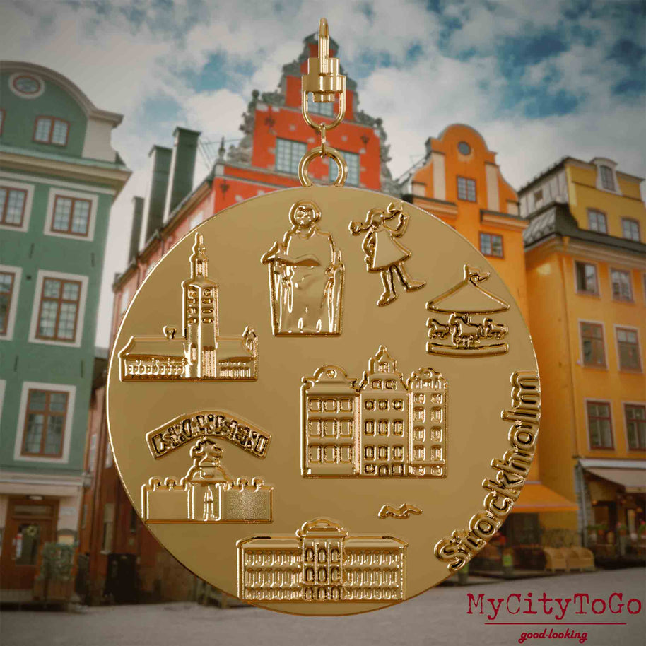 Halskette mit Drehwirbel und Rückseite eines vergoldeten Schmuckanhängers, auf dem Reliefs bekannter Sehenswürdigkeiten der Stadt Stockholm abgebildet sind. Den Hintergrund bildet eine Ansicht der Stadt Stockholm.
