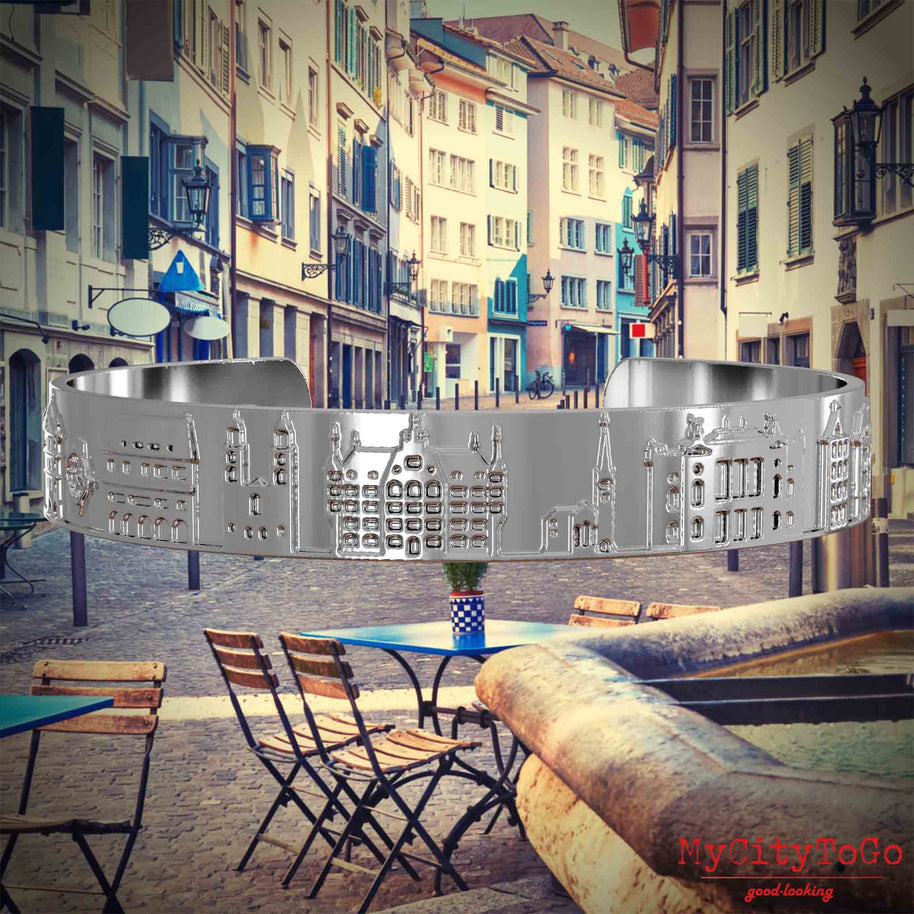 Versilberter Armreif mit Reliefs bekannter Sehenswürdigkeiten der Stadt Zuerich. Den Hintergrund bildet eine Ansicht der Stadt Zuerich.