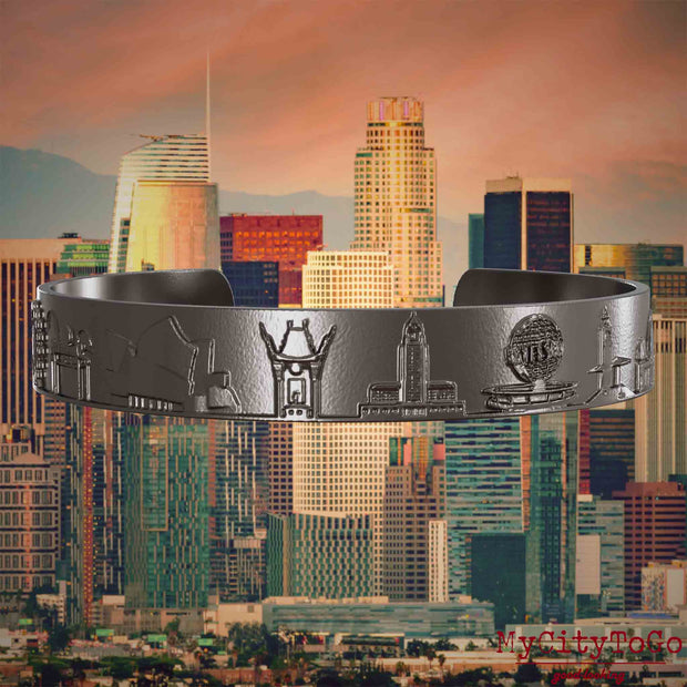 Armreif aus Titan mit Reliefs bekannter Sehenswürdigkeiten der Stadt Los Angeles. Den Hintergrund bildet eine Ansicht der Stadt Los Angeles.
