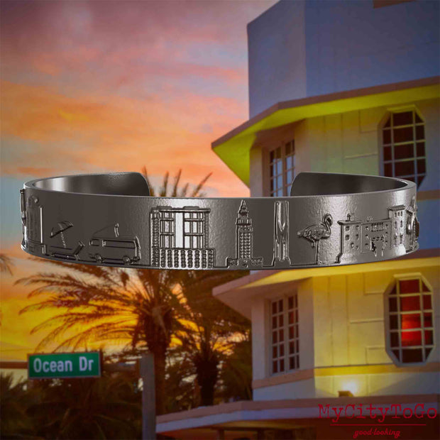 Armreif aus Titan mit Reliefs bekannter Sehenswürdigkeiten der Stadt Miami. Den Hintergrund bildet eine Ansicht der Stadt Miami.